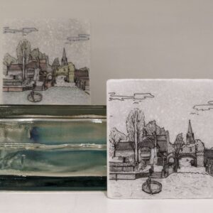 Two handmade ceramic tiles featuring illustrated riverside village scenes with a bridge, church spire, buildings and a small boat.