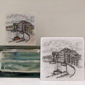 Two handmade ceramic tiles featuring illustrated harbour scenes with boats, buildings and waterfront detailing.