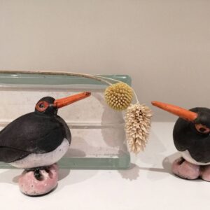Two handmade ceramic oystercatcher bird sculptures with black and white bodies and long orange beaks.