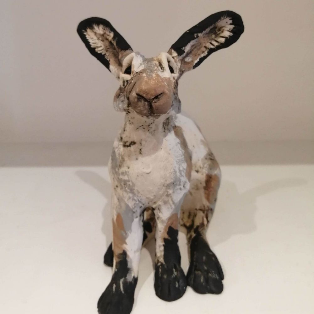 Handmade hare sculpture with white, brown and black painted detailing, long ears and seated pose.