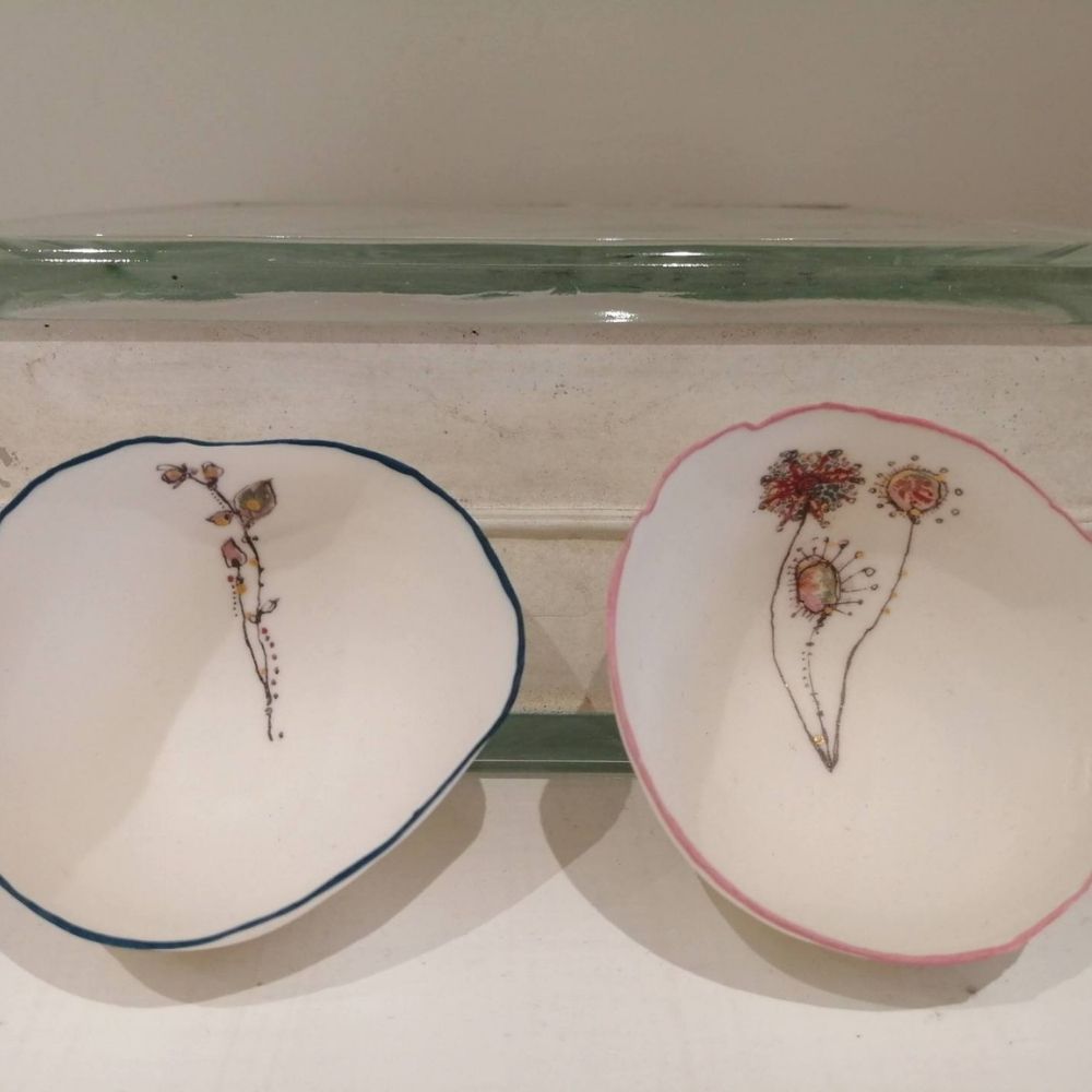 Two handmade white ceramic dishes with delicate hand-painted floral designs and blue and pink rims.