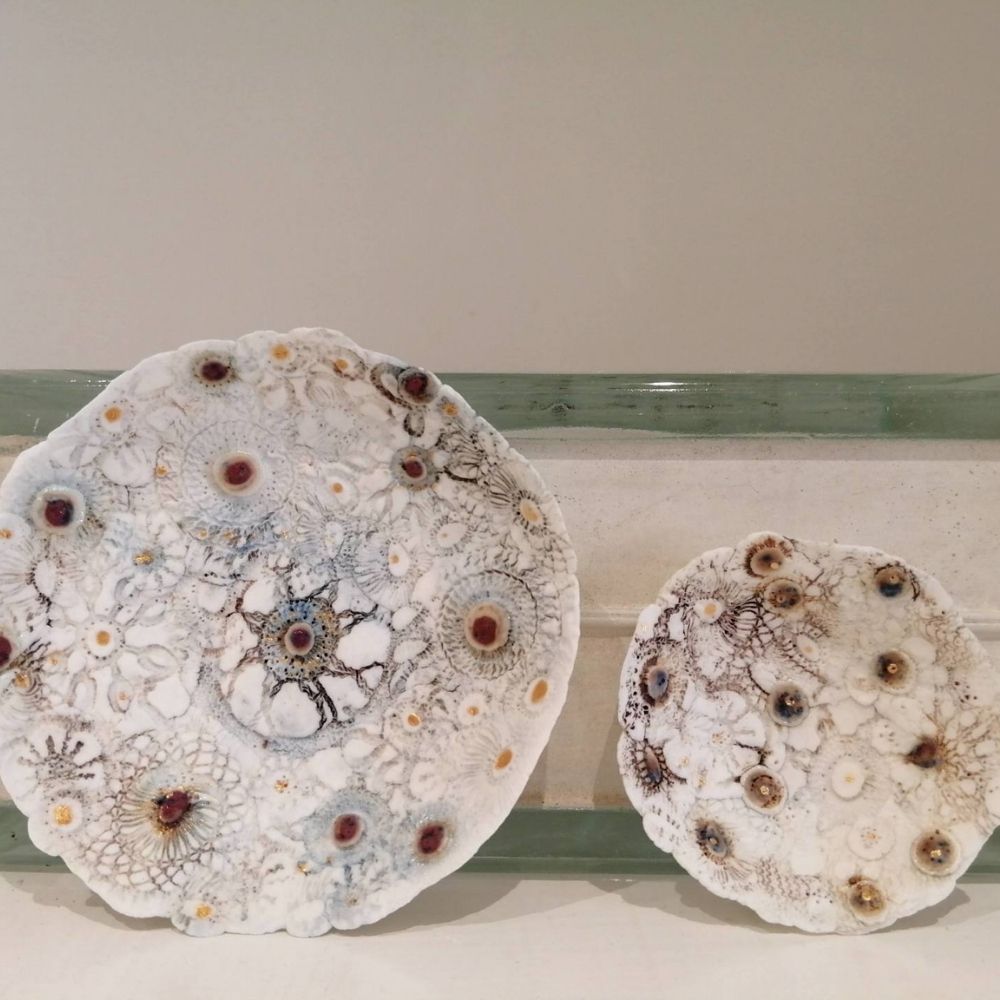 Two handmade white ceramic plates with textured floral and circular glazed detailing.