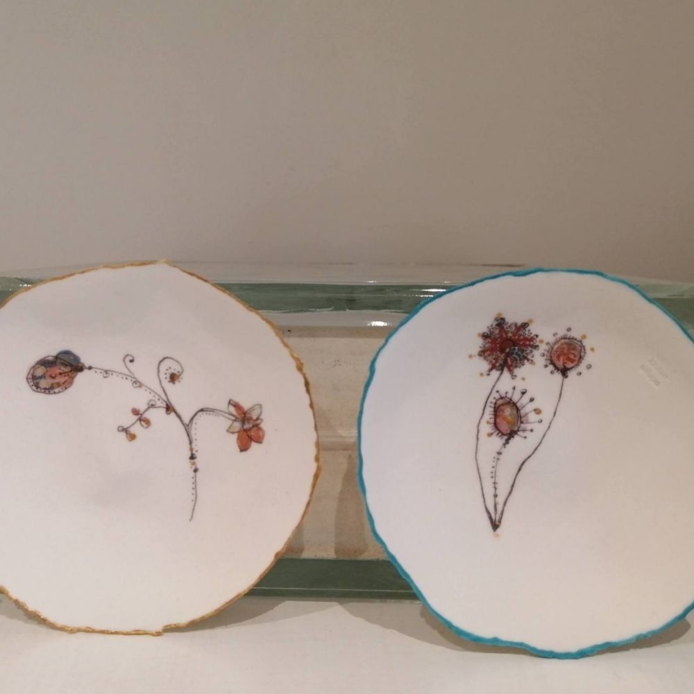 Two handmade white ceramic plates with delicate hand-painted floral designs and coloured rims.