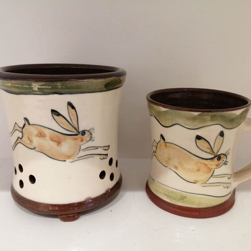 Two handmade ceramic pots with painted running hare designs, green detailing and dark brown rims.