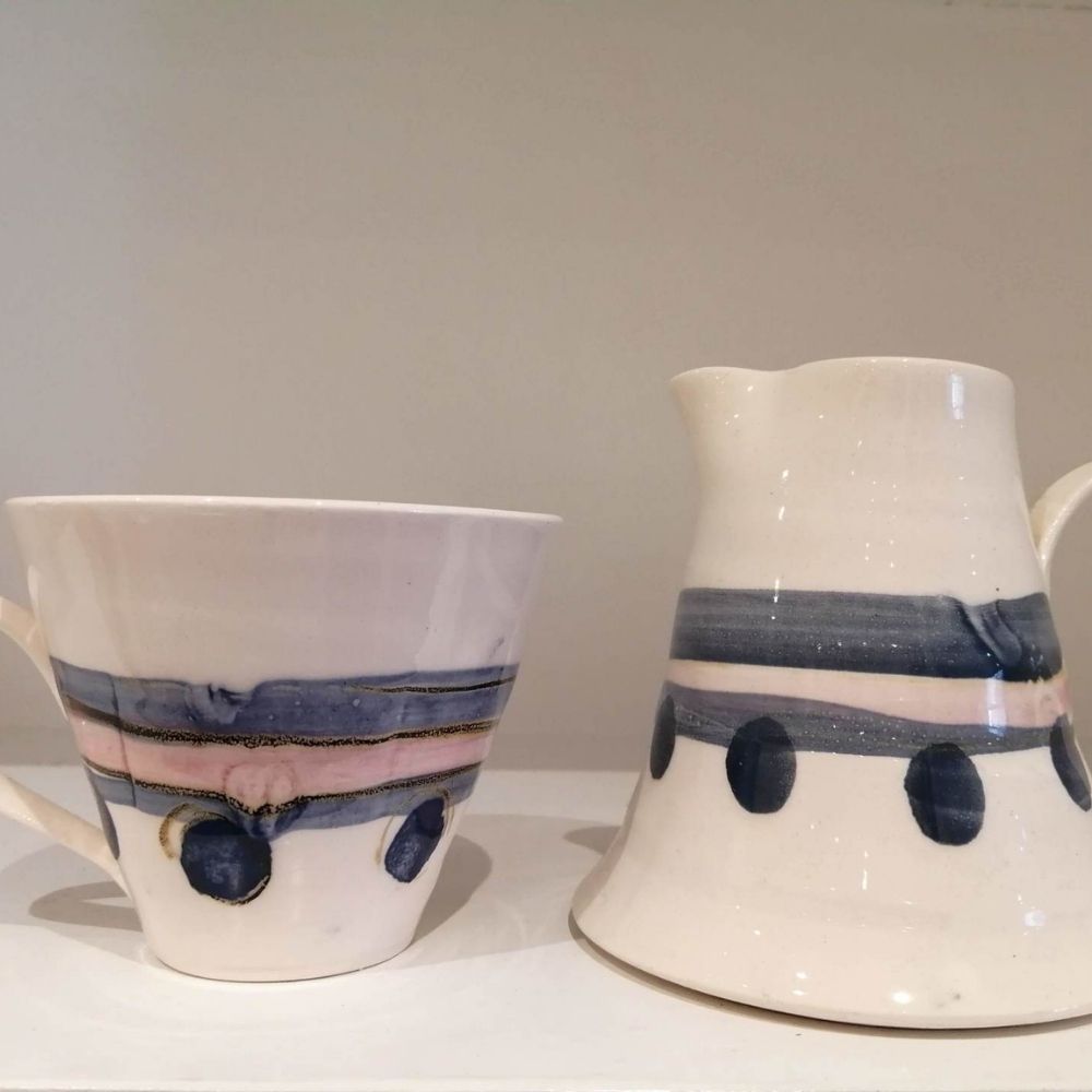 Handmade white ceramic jug and bowl with blue and pink striped decoration and dark circular accents.