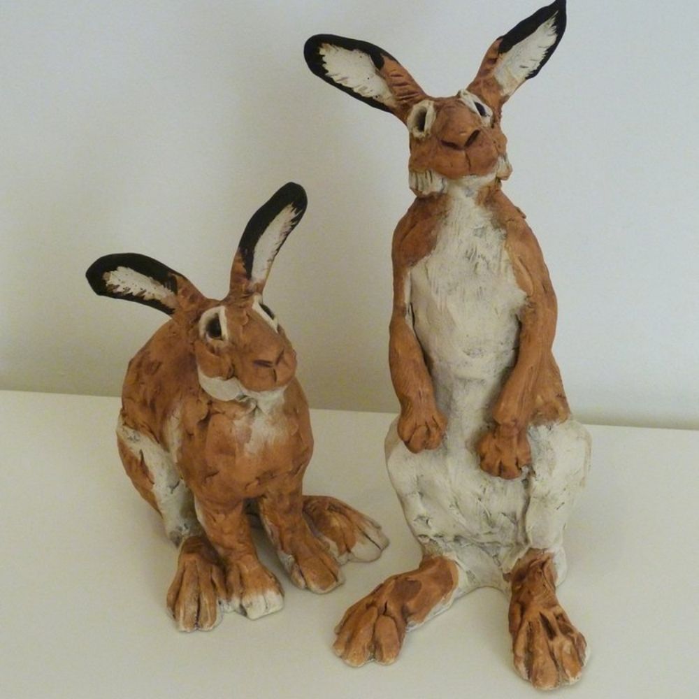 Two handmade brown and white hare sculptures displayed on a shelf.