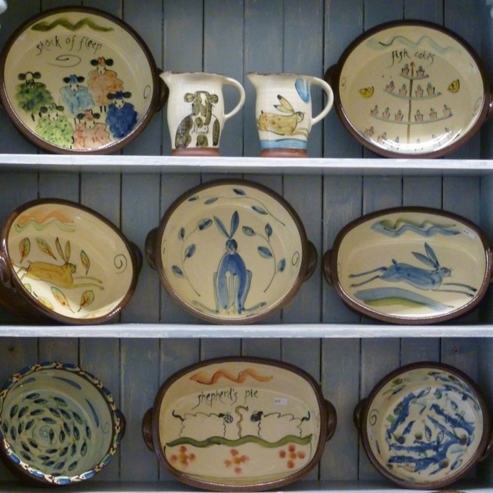 Handmade ceramic bowls and jugs displayed on shelves, featuring painted animal and food-themed designs.