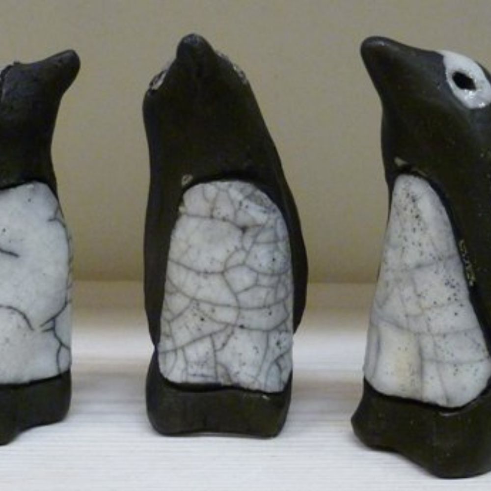 Three handmade black and white ceramic penguin sculptures displayed on a shelf.