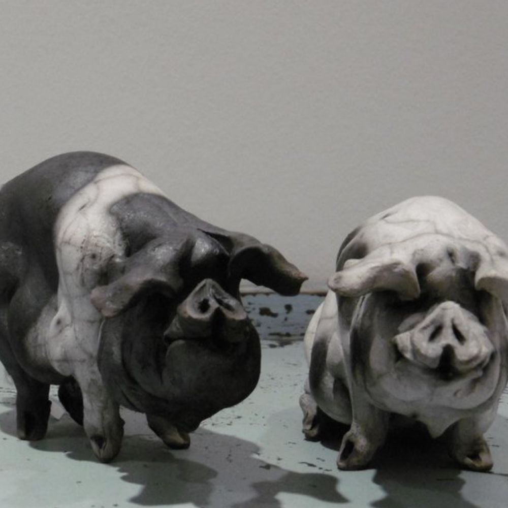 Two handmade ceramic pig figurines in black, white and grey tones displayed on a simple surface.