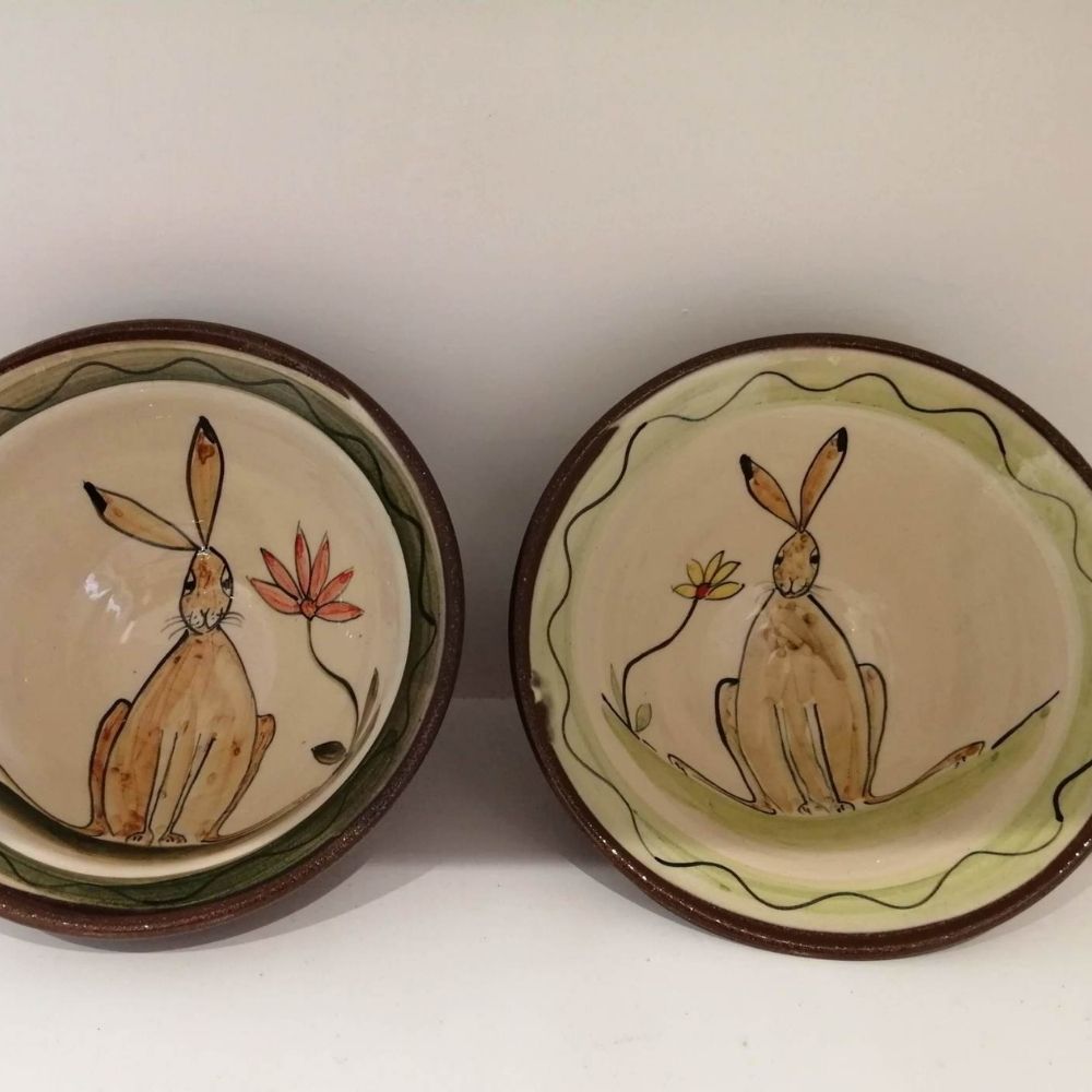 Two handmade ceramic bowls with hand-painted hare illustrations, floral details and dark brown rims.