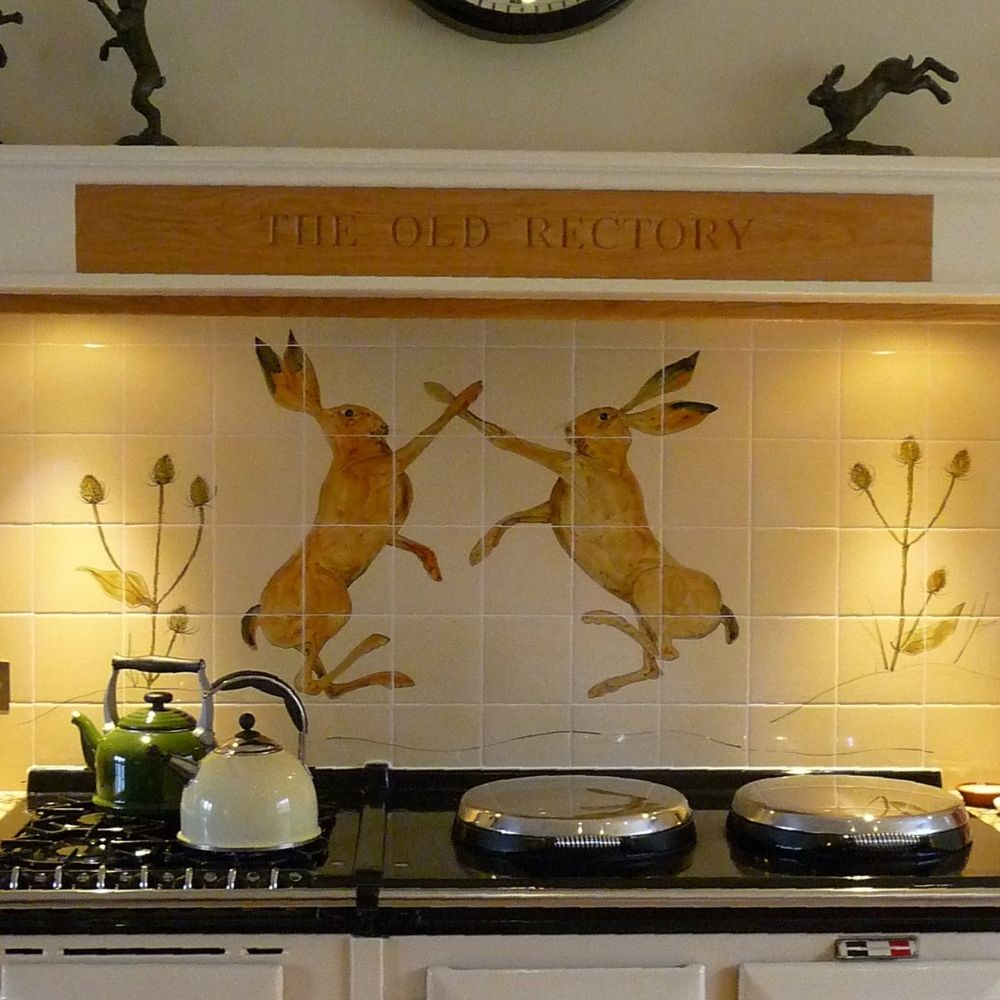 Decorative kitchen tile mural featuring two hand-painted boxing hares above a traditional range cooker.