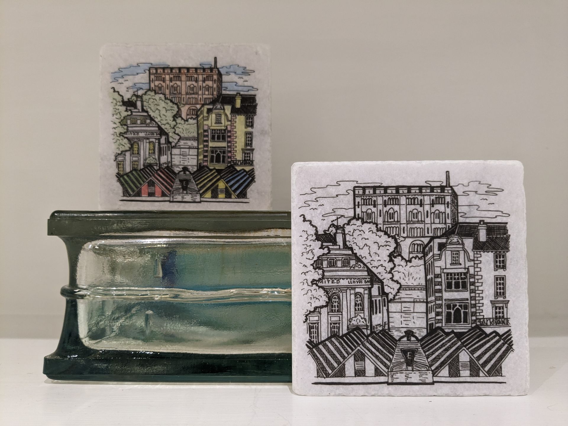 Two handmade ceramic tiles featuring illustrated cityscape scenes with historic buildings, steps and rooftops.