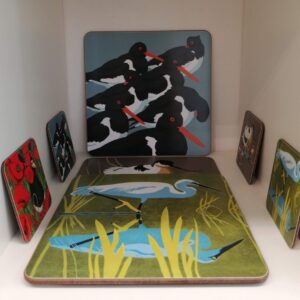 Display of illustrated placemats and coasters featuring oystercatchers, an egret and other bird designs.