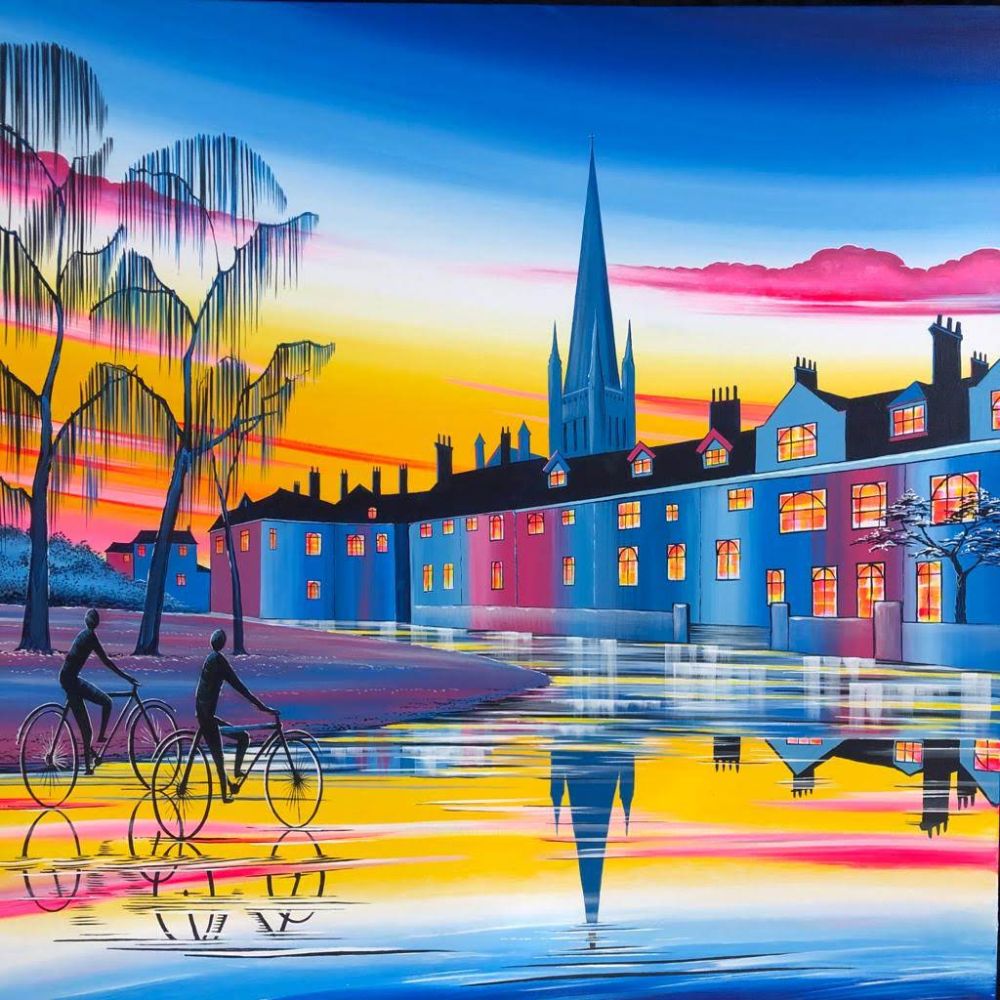 Bright riverside artwork featuring cyclists, a church spire, glowing townhouses and colourful sunset reflections on the water.
