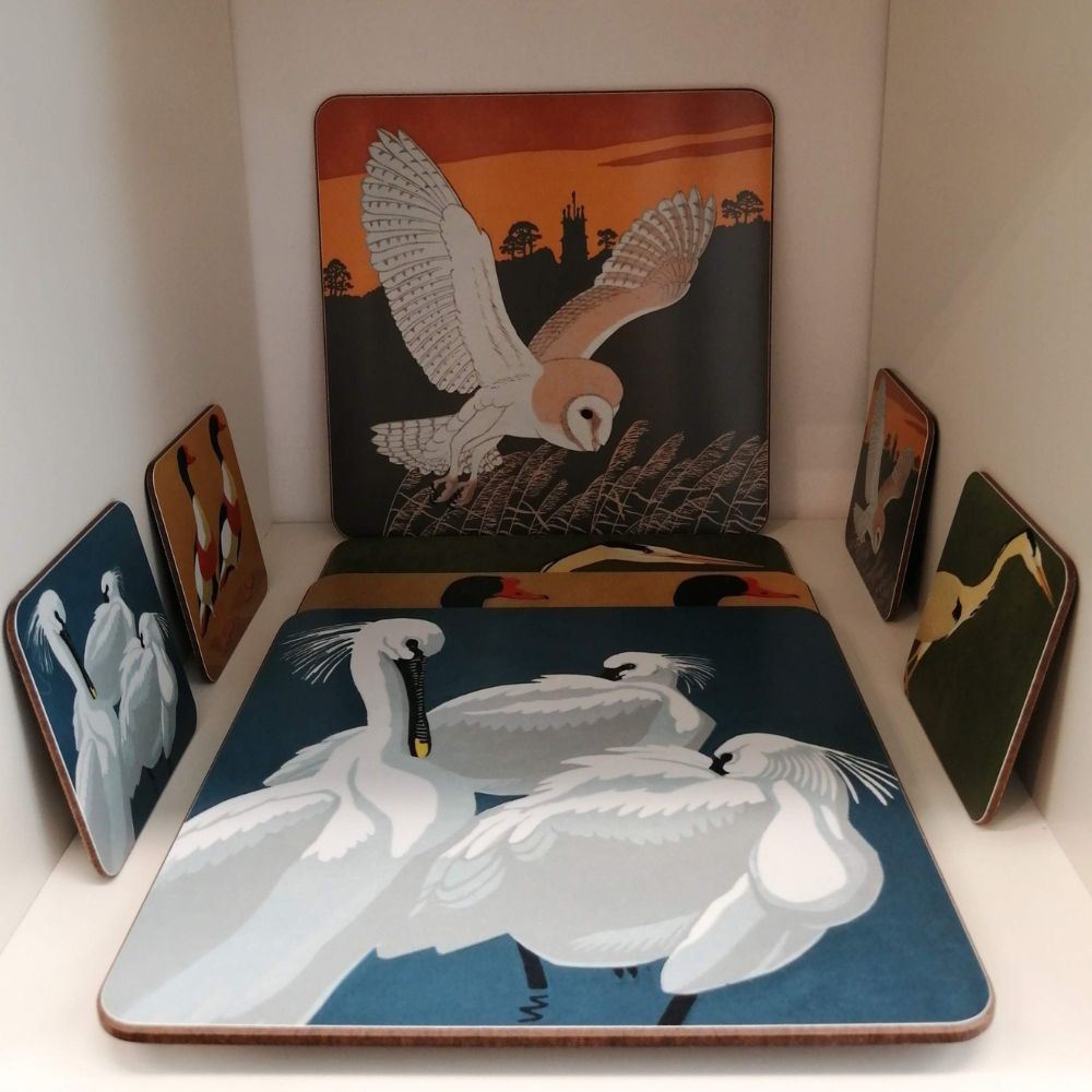 Display of illustrated placemats and coasters featuring spoonbills, barn owl, egret and other bird designs.