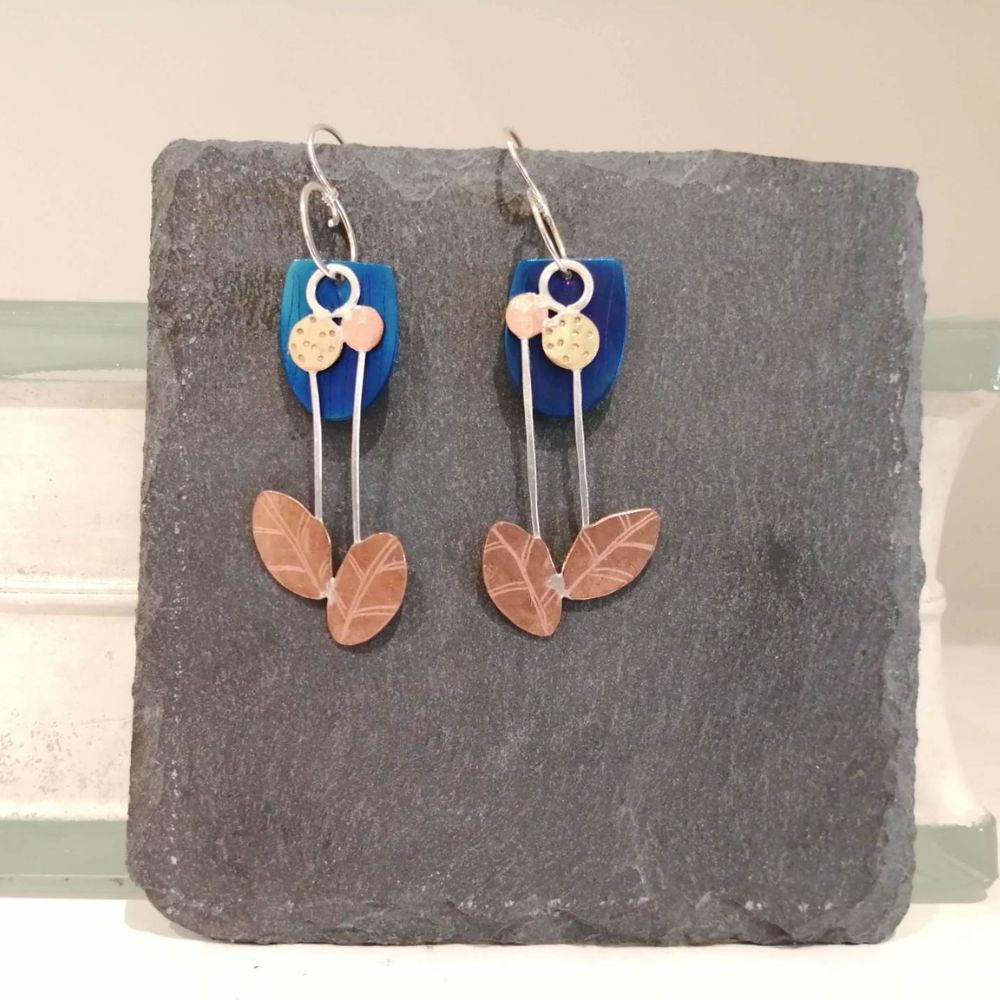 Pair of handmade drop earrings with blue, copper and gold leaf details displayed on a dark slate background.