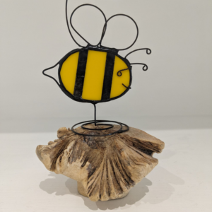 Handmade stained glass bee decoration with yellow and black striped body, wire wings and antennae, displayed on natural wood.