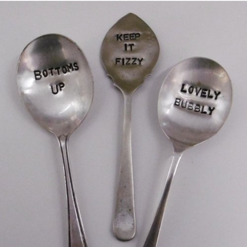Three hand stamped vintage spoons with messages reading Bottoms Up, Keep It Fizzy and Lovely Bubbly.