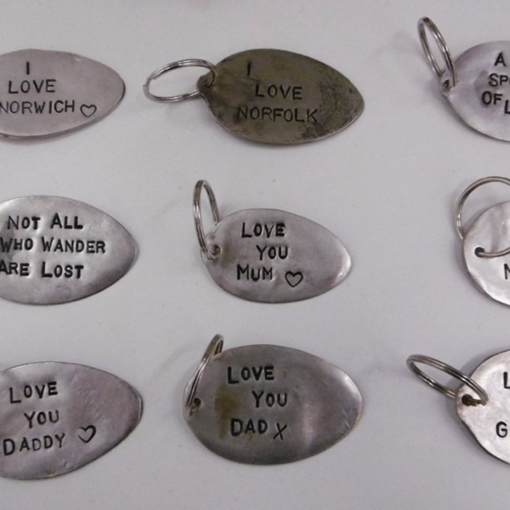 Hand stamped oval metal keyrings with personalised messages including I love Norfolk and love you dad.