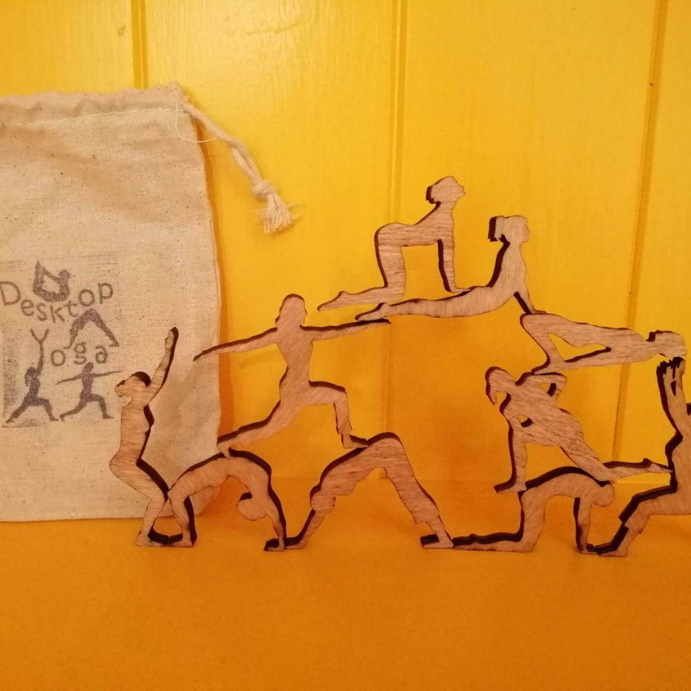 Wooden desktop yoga balancing game with cut-out yoga pose figures arranged beside a cotton drawstring bag.