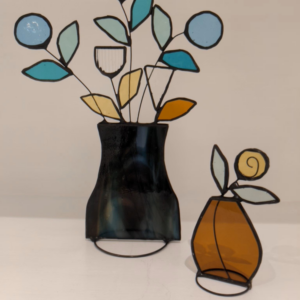 Handmade stained glass vase with abstract flowers displayed beside an amber fruit decoration with leaf and spiral detail.