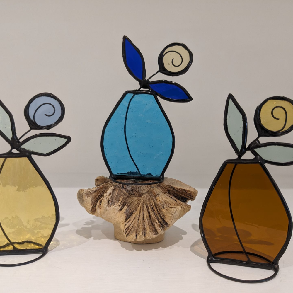 Handmade stained glass fruit decorations in yellow, blue and amber tones with leaf and spiral details, displayed on natural wood.