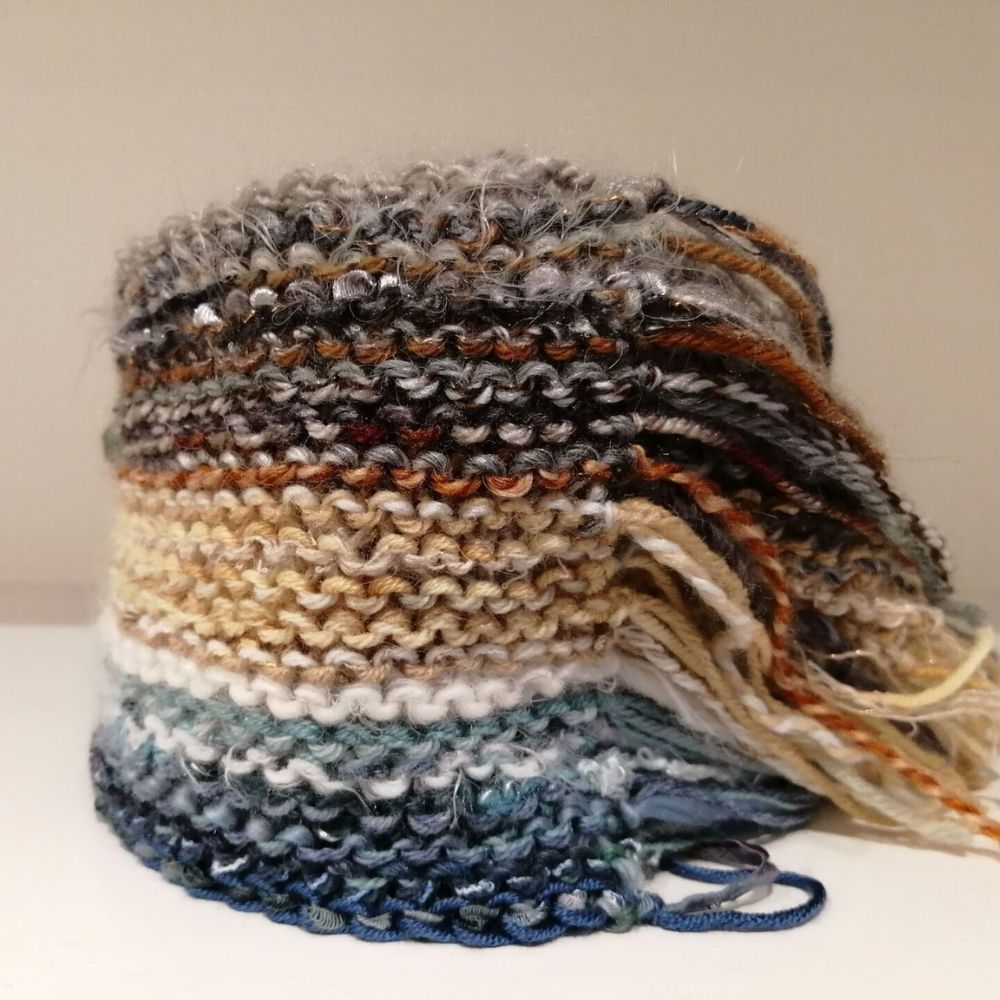 Close-up of a hand-knitted striped wool scarf with layered earthy tones, textured stitching and loose yarn ends.a