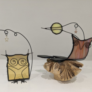Handmade stained glass owl and bird decorations with wire details, star charms and a moon design displayed on natural wood.