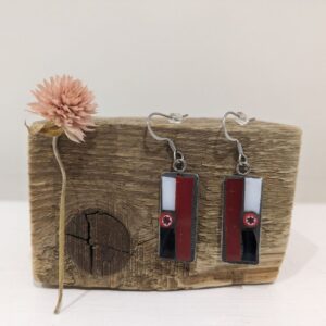 Pair of handmade rectangular drop earrings with red, black and white cassette-inspired details displayed on rustic wood.