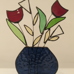 Stained glass flower arrangement with red, white and green flowers displayed in a dark blue glass vase.