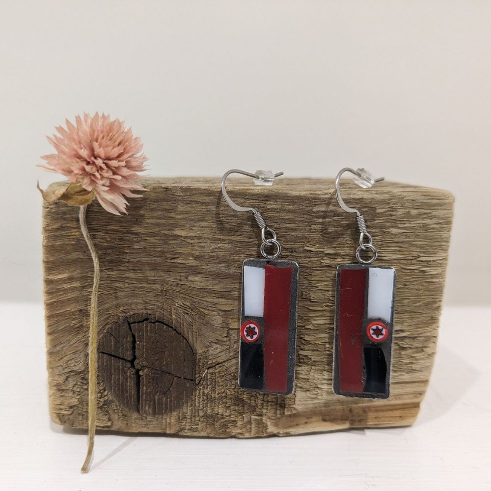 Pair of handmade rectangular drop earrings with red, black and white cassette-inspired details displayed on rustic wood.