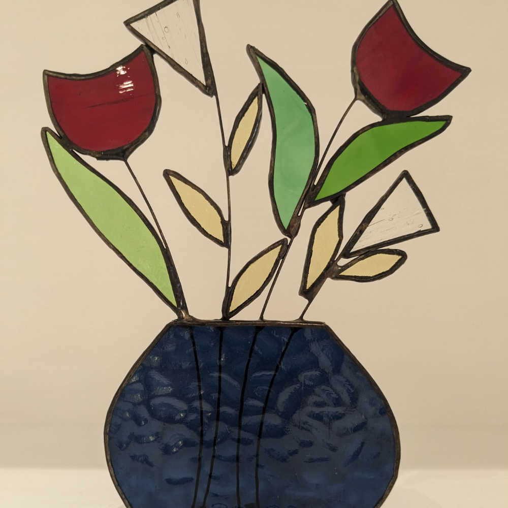 Stained glass flower arrangement with red, white and green flowers displayed in a dark blue glass vase.